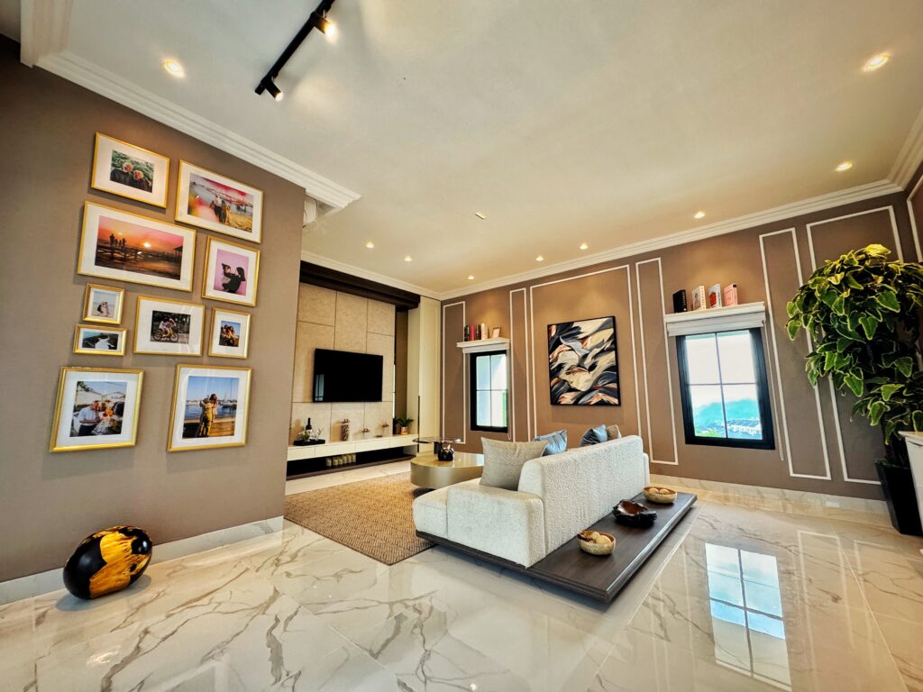 Modern living room with a gallery wall of framed photos on a taupe wall, white molding, and track lighting over a beige rug and marble floor.