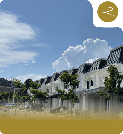 Row of white townhouses with black gabled roofs on a sunny street, with trees and a blue sky.